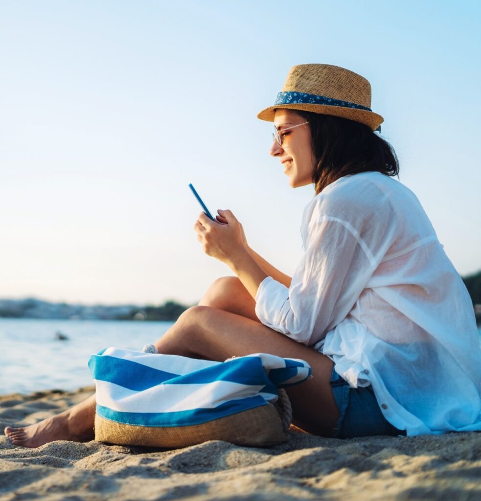 A women using phone at the beach while traveling Image by urbazon from Getty Images Signature